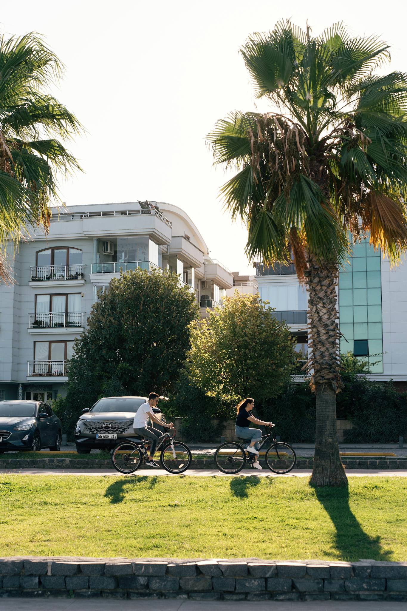 Two people biking in a modern city setting with palm trees. Urban lifestyle and outdoor recreation.