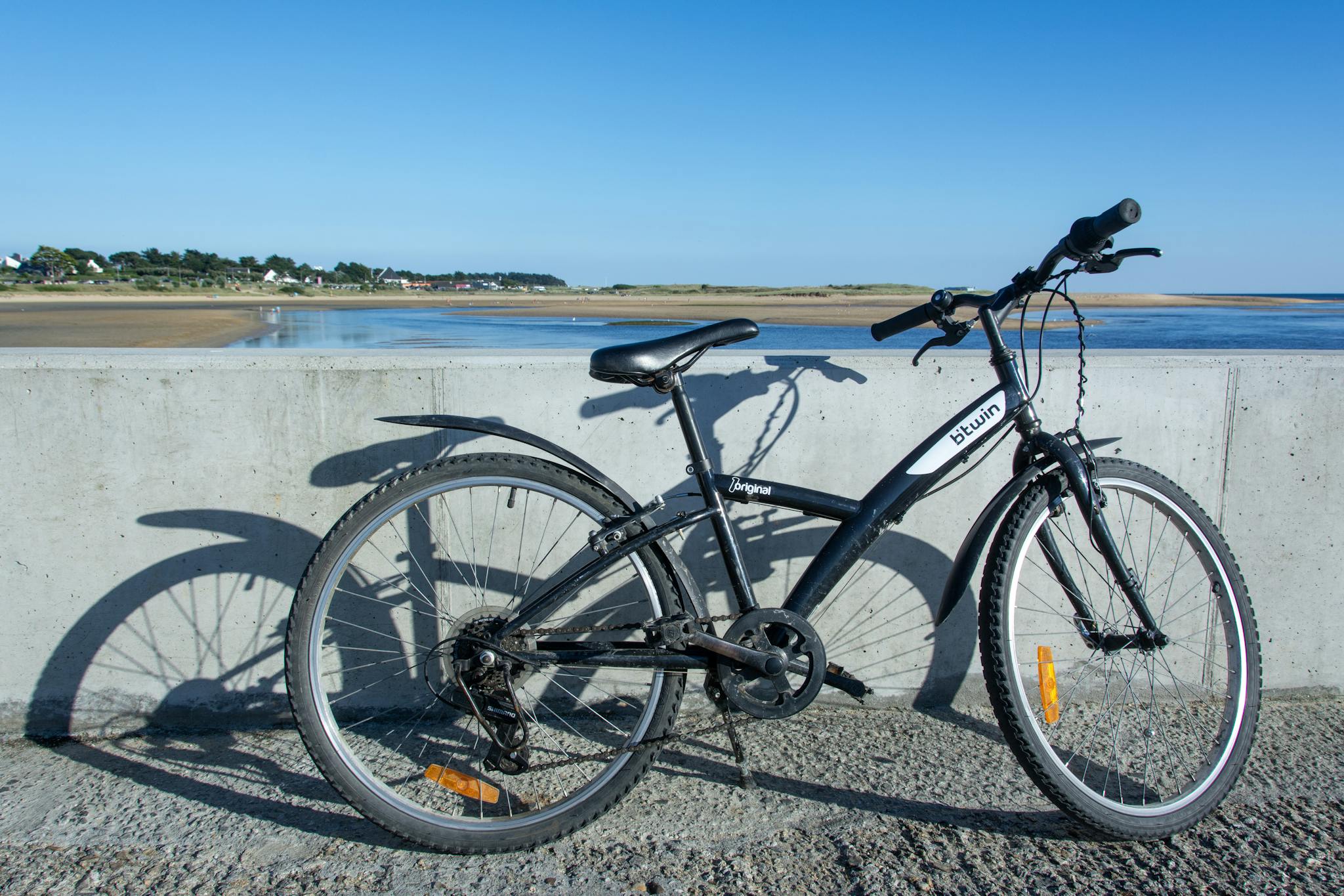 A bicycle parked by the seashore with a tranquil sea and clear blue sky in the background.