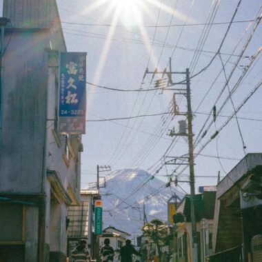 Three cyclists walk their bikes on a street with Mount Fuji visible in the background.