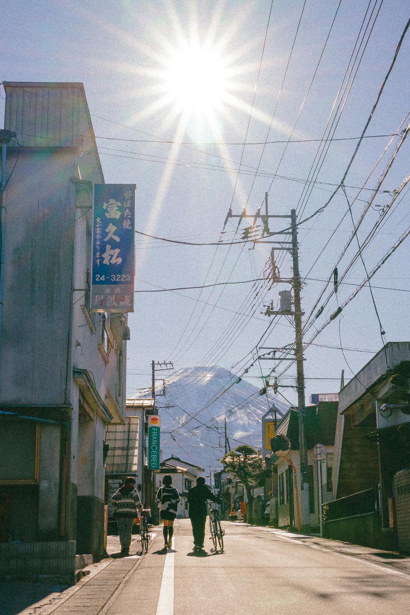 Three cyclists walk their bikes on a street with Mount Fuji visible in the background.